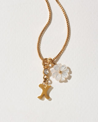 Gold necklace with a flower and 'X' charm on a light background