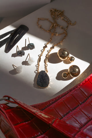 Jewelry including earrings and a necklace on a white surface with a red handbag.