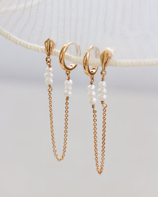 Gold hoop earrings with pearl beads on gold chains on a white background