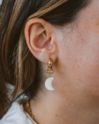Closeup of woman wearing crescent moon shaped mother-of-pearl gold hoop earring.