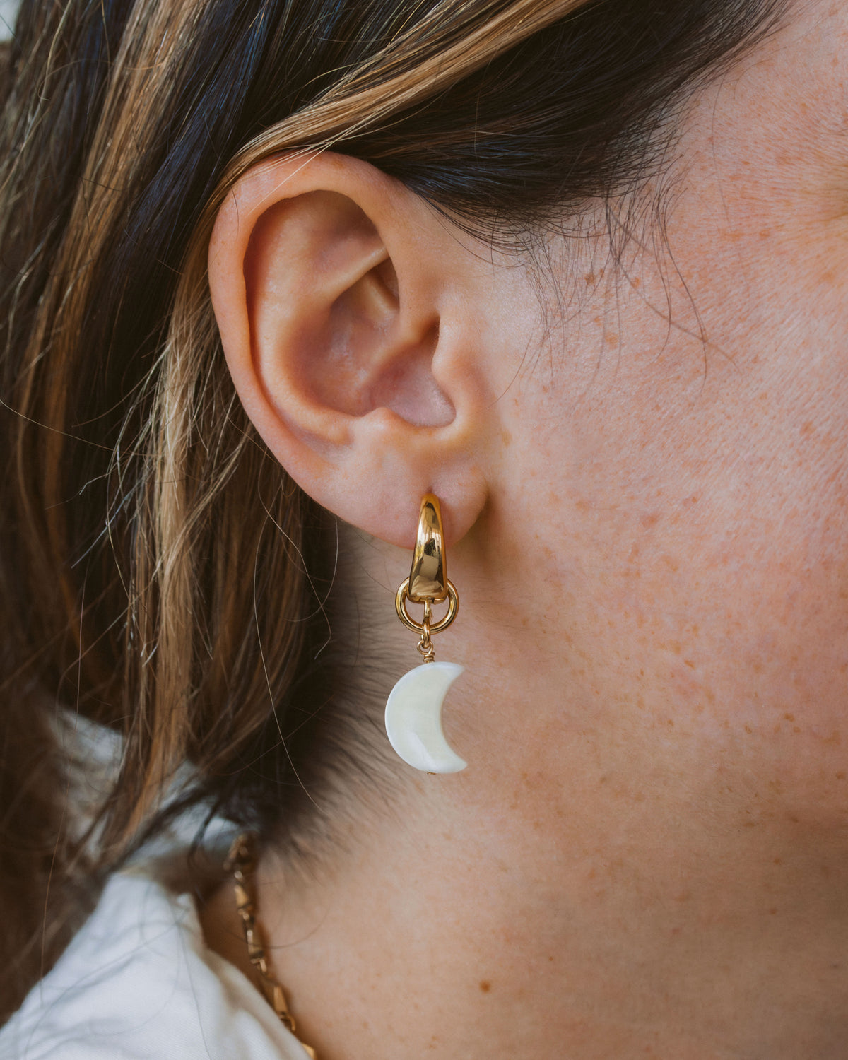 Closeup of woman wearing crescent moon shaped mother-of-pearl gold hoop earring.