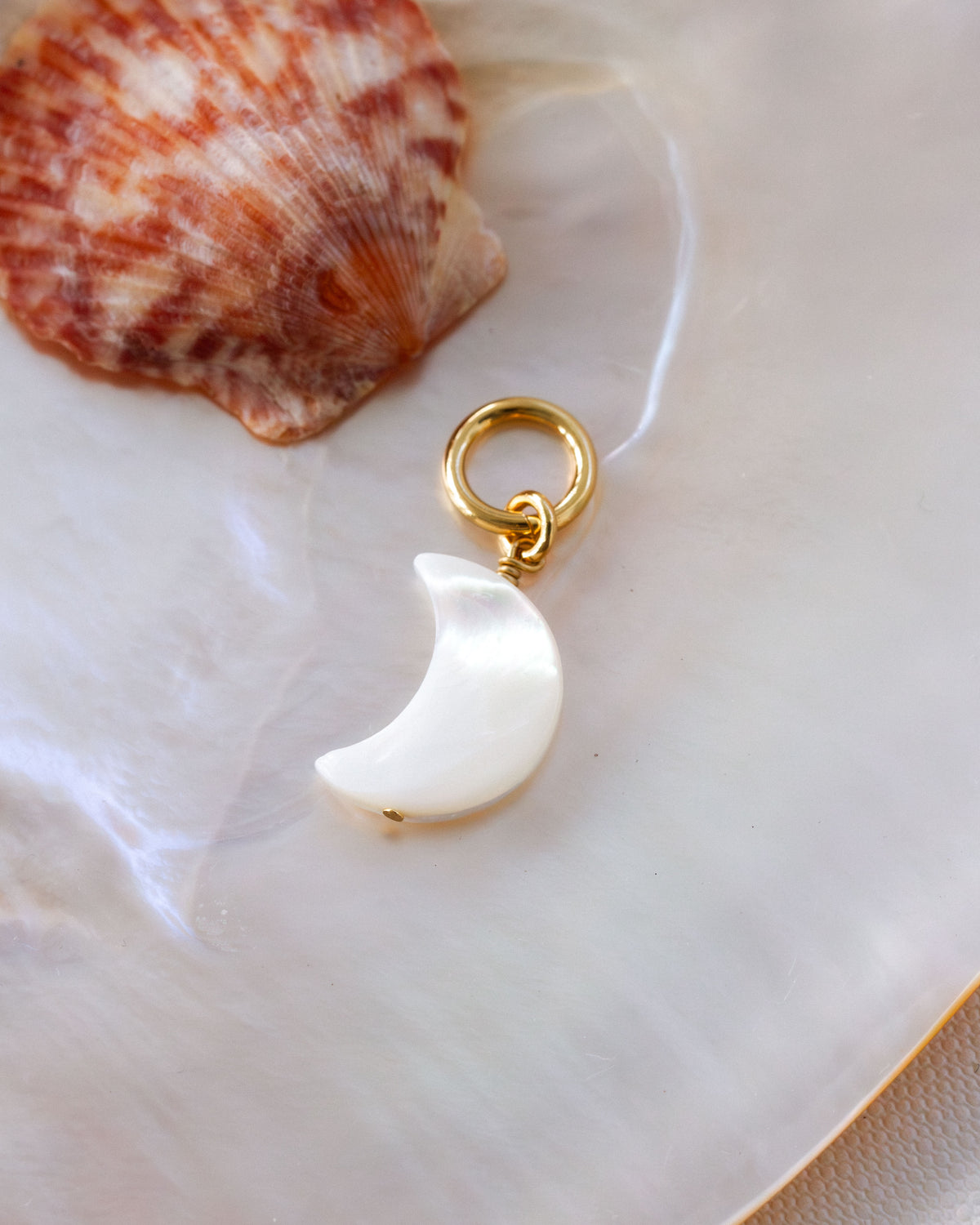 Moon shaped mother of pearl gold hoop earring laying on a shiny shell surface.