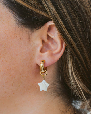 Closeup of woman wearing star shaped mother of pearl gold hoop earring.