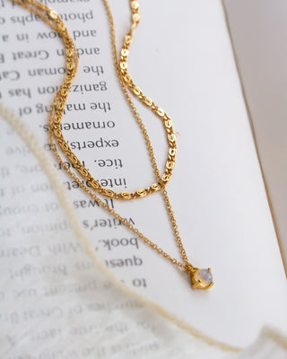 Layering gold necklace with a small opal pendant on an open book