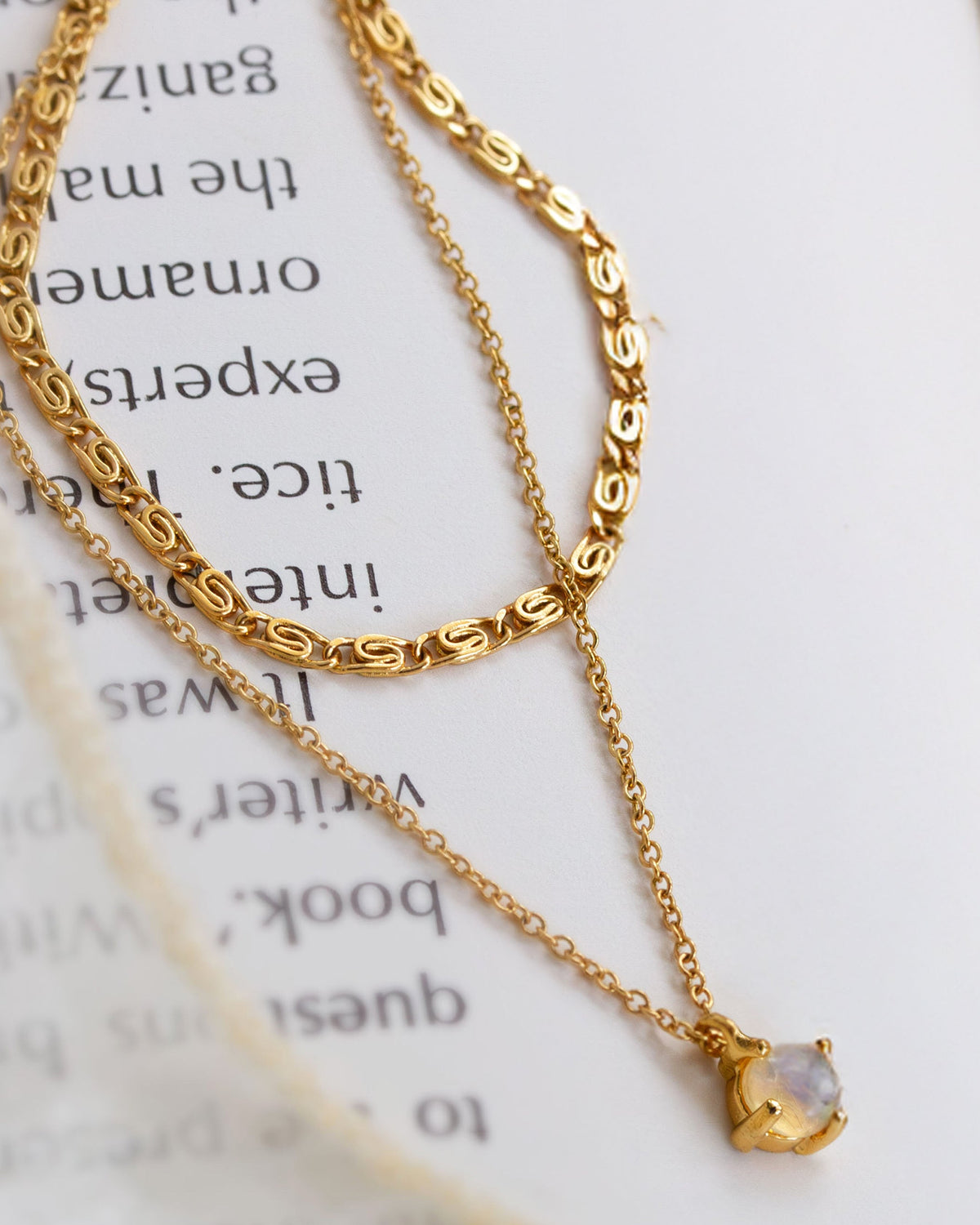 Layering gold necklace with a small opal pendant on an open book