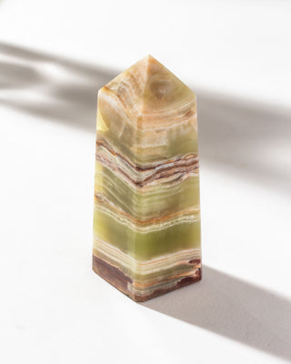 Large Calcite crystal obelisk standing on a white surface.