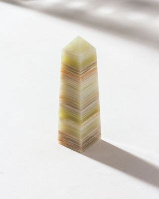 Calcite obelisk crystal with natural banded patterns, placed on a light surface.