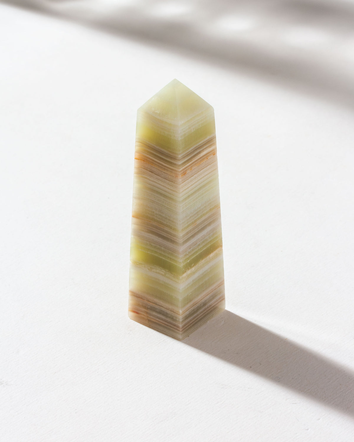 Calcite obelisk crystal with natural banded patterns, placed on a light surface.