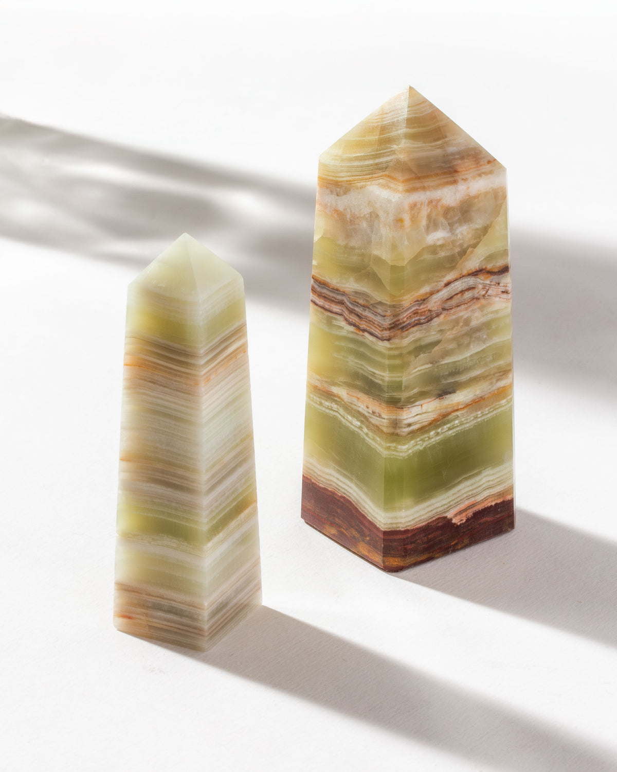 Medium and large calcite obelisks standing next to each other on a white surface.