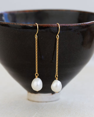 Pearl earrings with gold chains on a black ceramic bowl