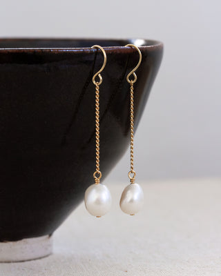 Pearl earrings with gold hooks on a neutral background