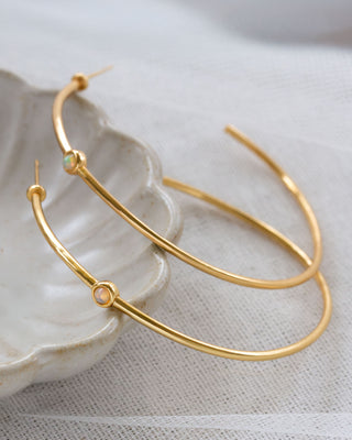 Gold hoop earrings on a textured white surface with small opal gemstone.