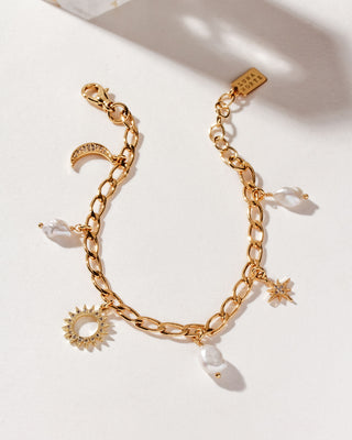 A gold-tone charm bracelet featuring a crescent moon, a star, and a sunburst pattern, with white pearl drops, displayed against a neutral background.