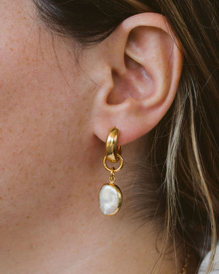 Person wearing oval-shaped pearl charm with gold-colored hoop closure.