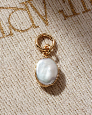 Rounded mother of pearl earring charm on gold hoop, place on a canvas fabric surface.