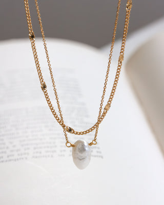 Gold chain layering necklace with a white mother of pearl pendant on a light background