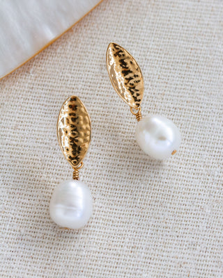 Gold and pearl earrings on a textured beige surface