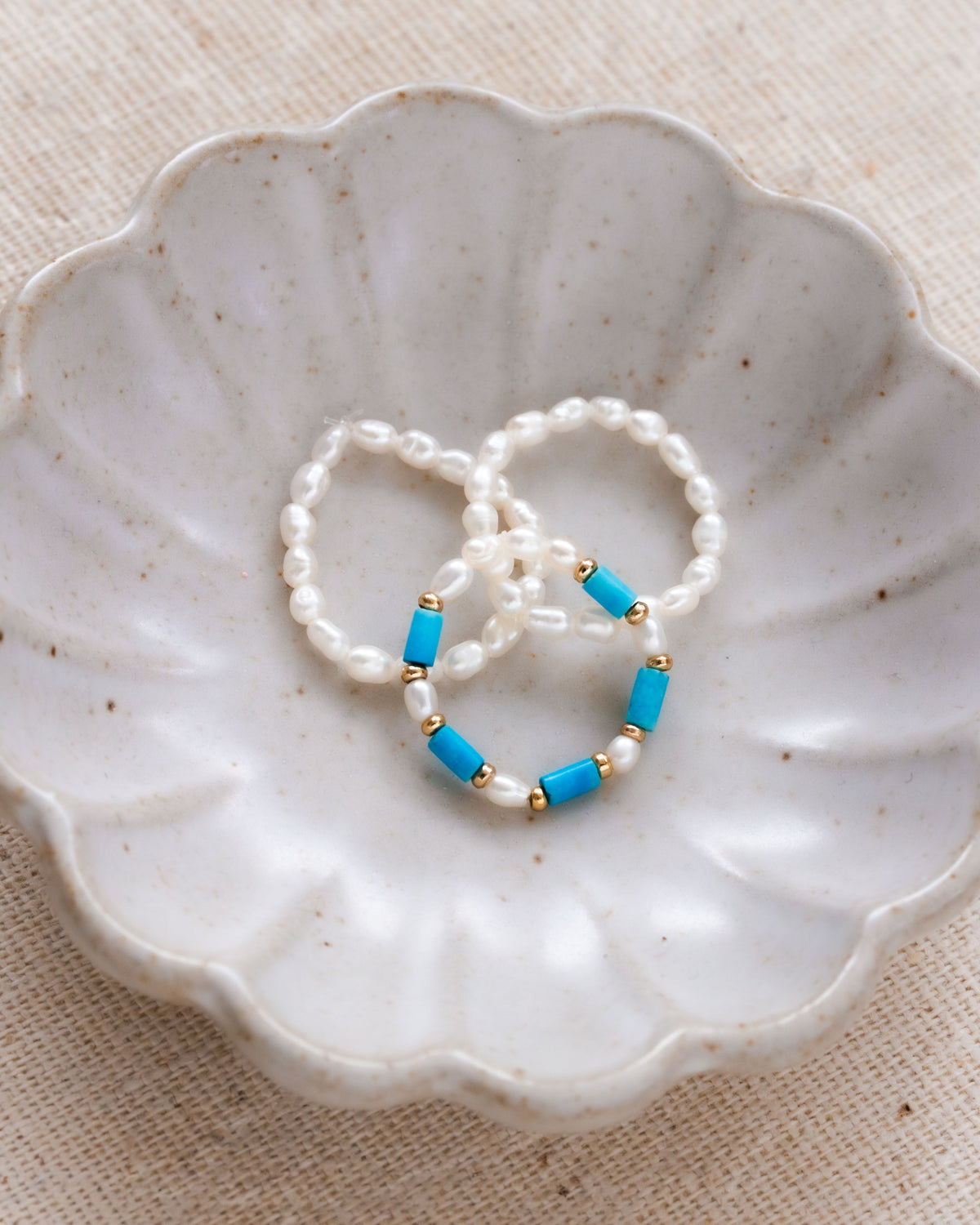 Three stacked pearl and turquoise stretch rings on a scalloped dish