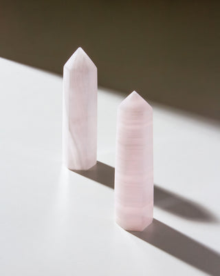 Two pink calcite gemstone towers are placed on a flat surface, displaying their striped patterns.