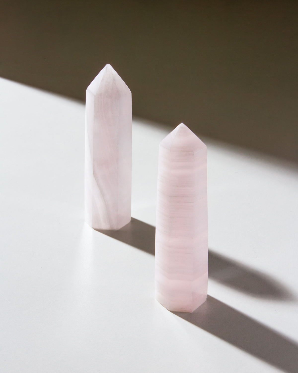 Two pink calcite gemstone towers are placed on a flat surface, displaying their striped patterns.