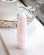 Pinkish striped calcite gemstone obelisk tower on a white window sill