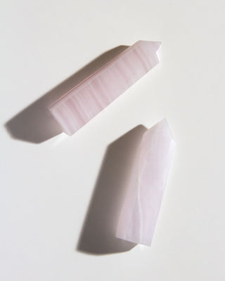 Two pink striped calcite gemstone towers laying on a white surface.