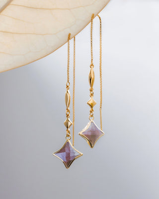 Gold star shaped earrings with coffee moonstone gemstones hanging against a neutral background