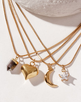 A collection of gold-toned snake chain necklaces with various charms, displayed against a neutral background.