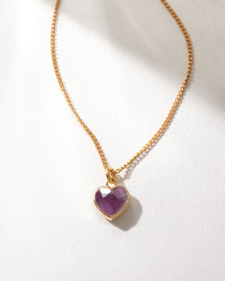 Gold necklace with a heart-shaped purple amethyst gemstone pendant on a white background