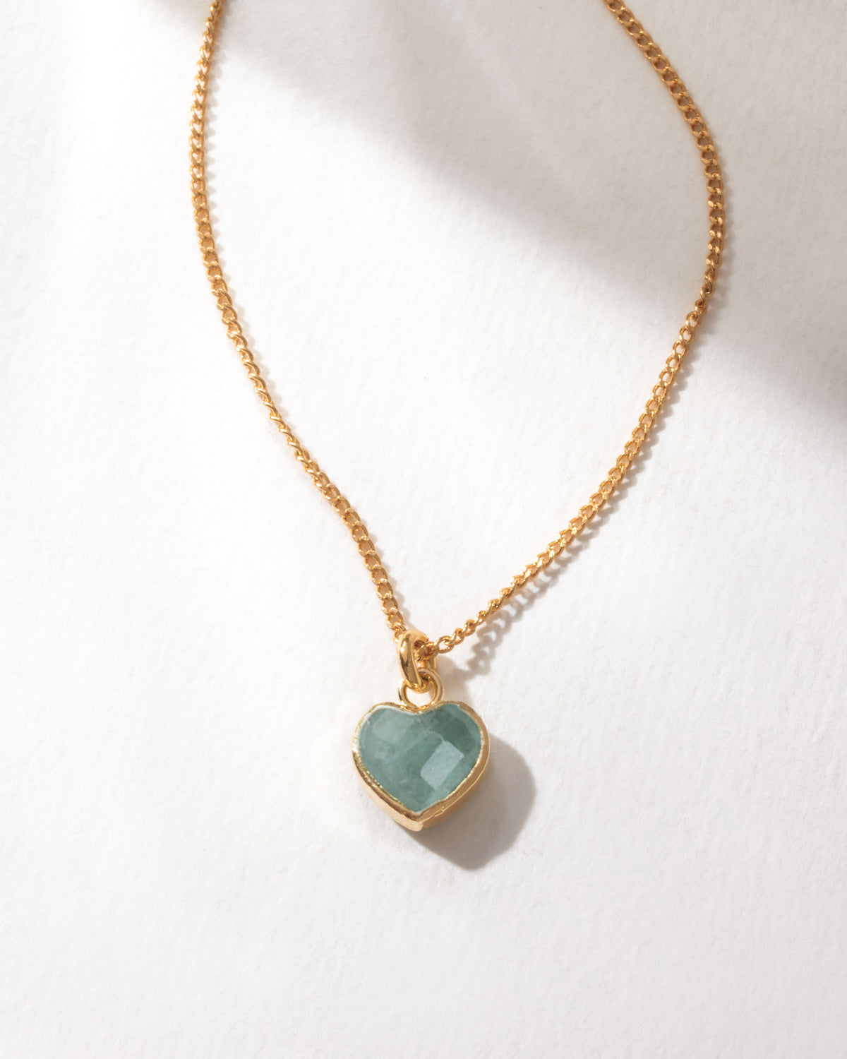 Gold necklace with a heart-shaped green aquamarine pendant on a white background