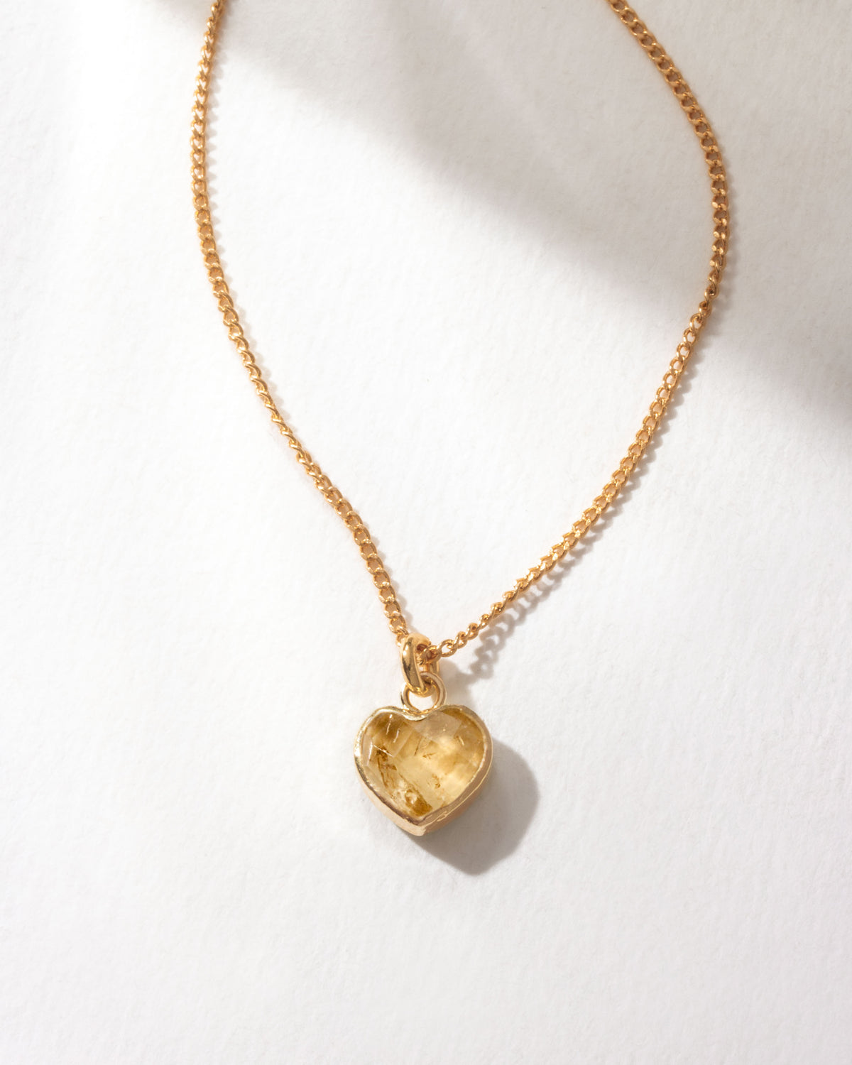 Gold necklace with a heart-shaped citrine pendant on a white background