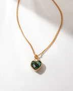 Gold necklace with a dark green emerald heart-shaped pendant on a white background