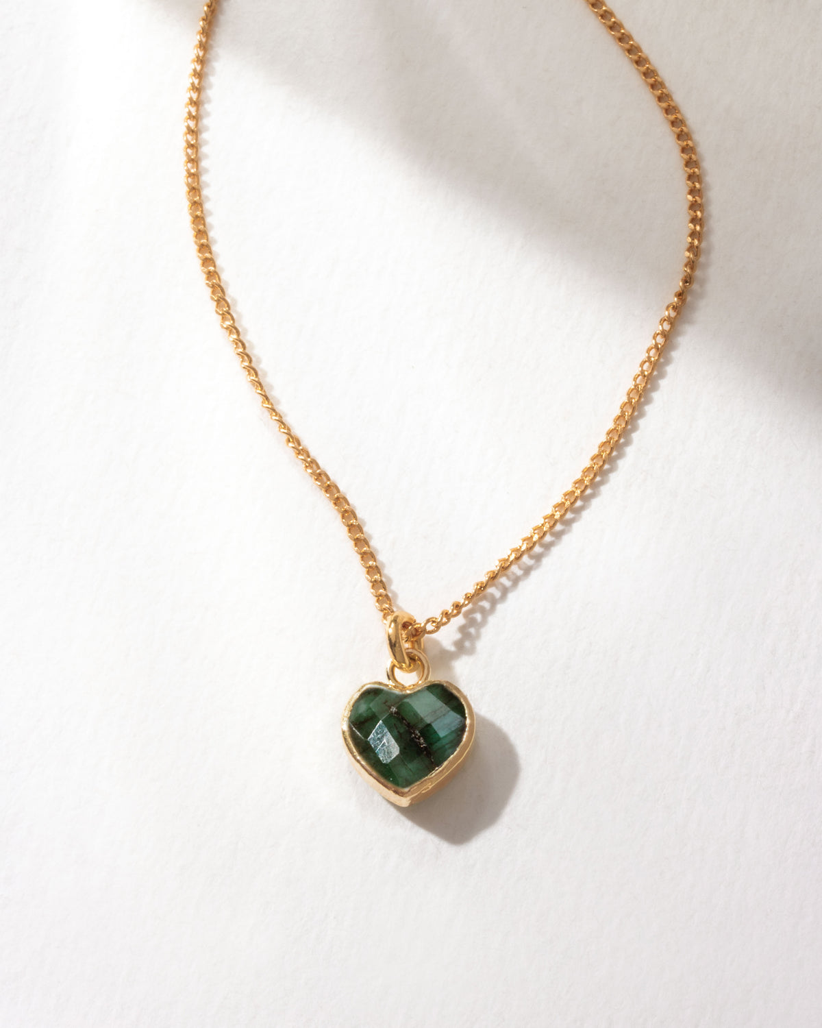 Gold necklace with a dark green emerald heart-shaped pendant on a white background