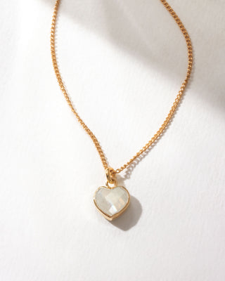 Gold necklace with a heart-shaped moonstone pendant on a white background