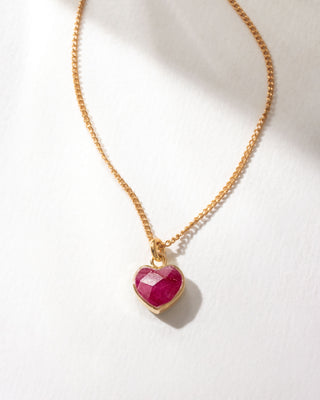Gold necklace with a red ruby heart gemstone pendant on a white background
