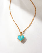 Gold necklace with a turquoise heart-shaped pendant on a white background