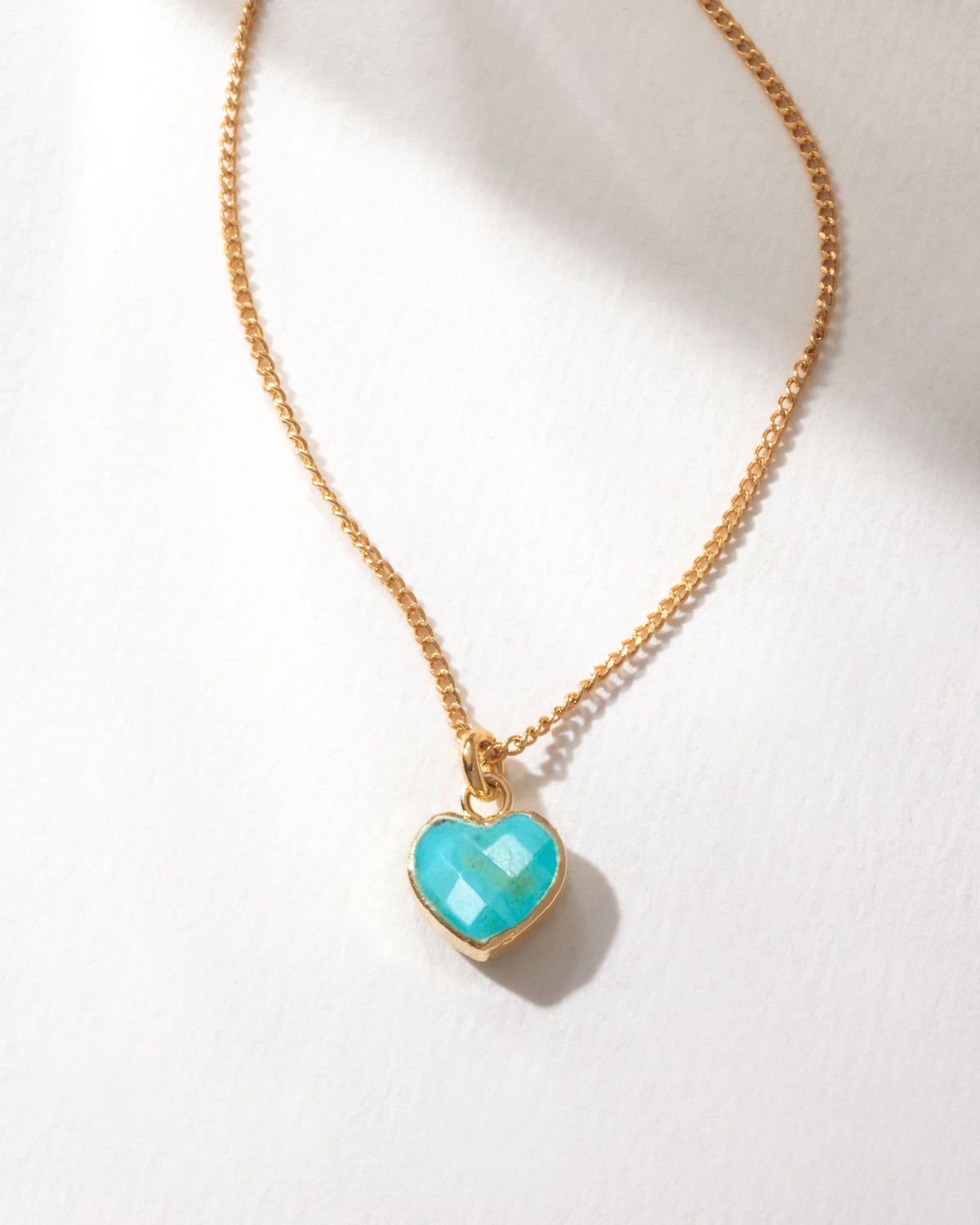 Gold necklace with a turquoise heart-shaped pendant on a white background