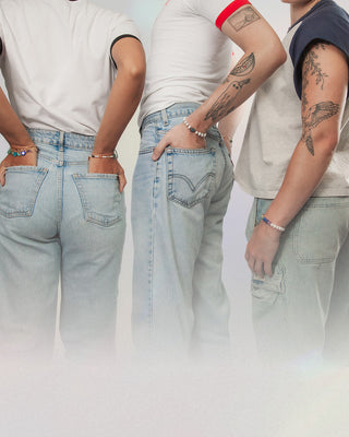 Three people wearing light blue jeans and genuine gemstone and pearl bracelets with a neutral background