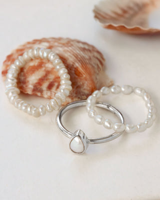 Two pearl stretch rings and silver ring with a teardrop mother of pearl on a white background with shells.