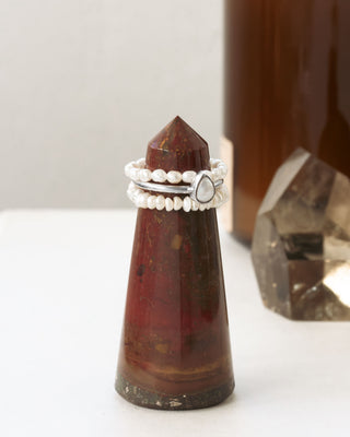 Two pearl stretch rings with one silver ring with mother of pearl teardrop on a reddish brown gemstone tower with a blurred background