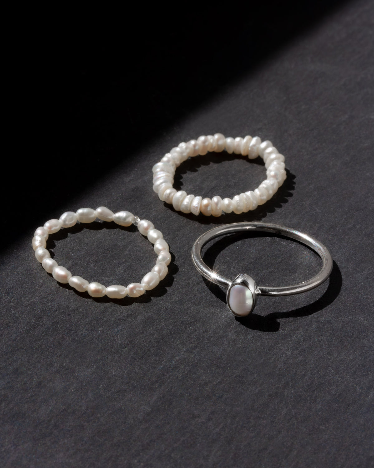 Three pearl rings on a dark surface