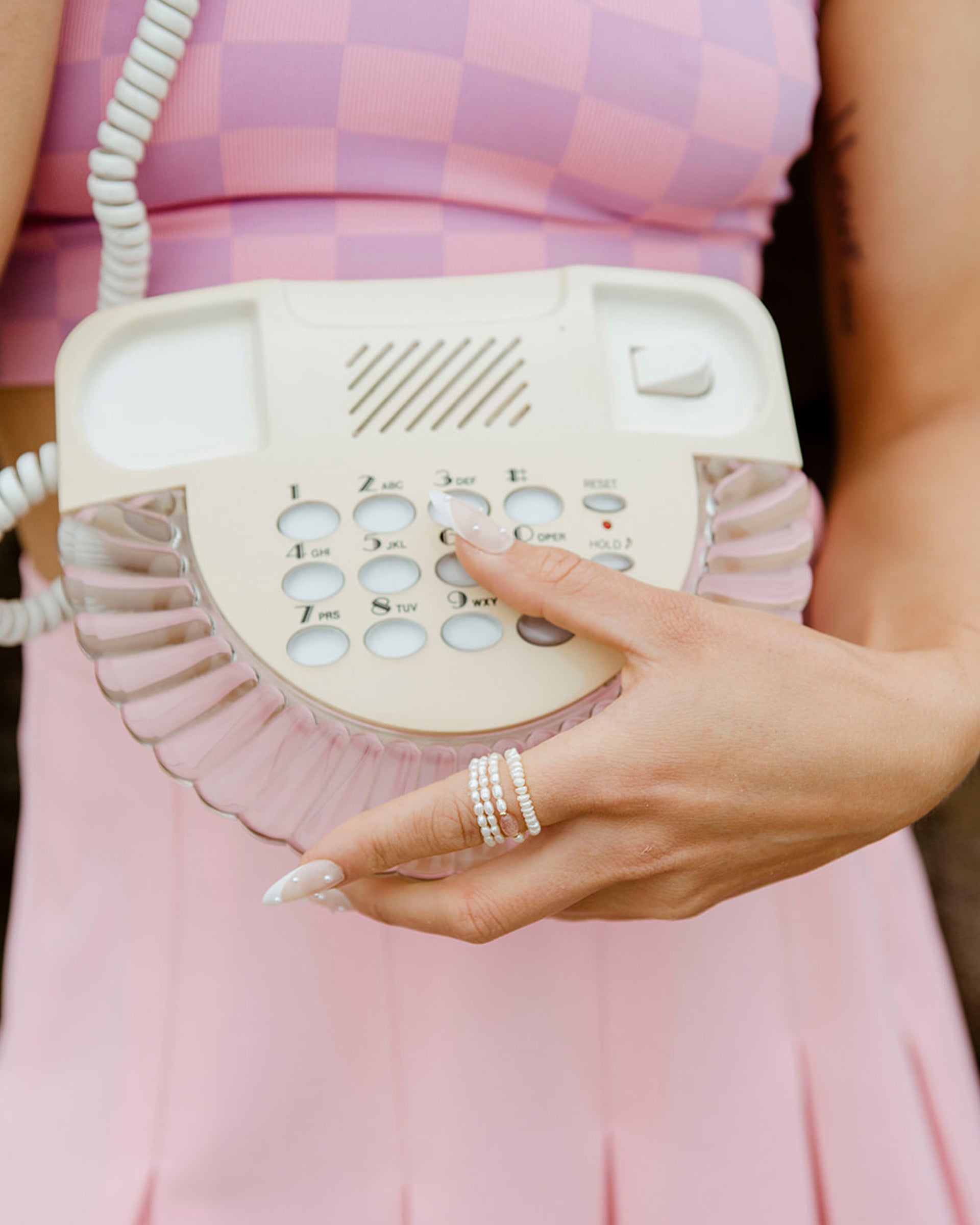 Three Coastal Stretch Rings, one Strawberry Quartz, are worn on a hand dialing a retro telephone.