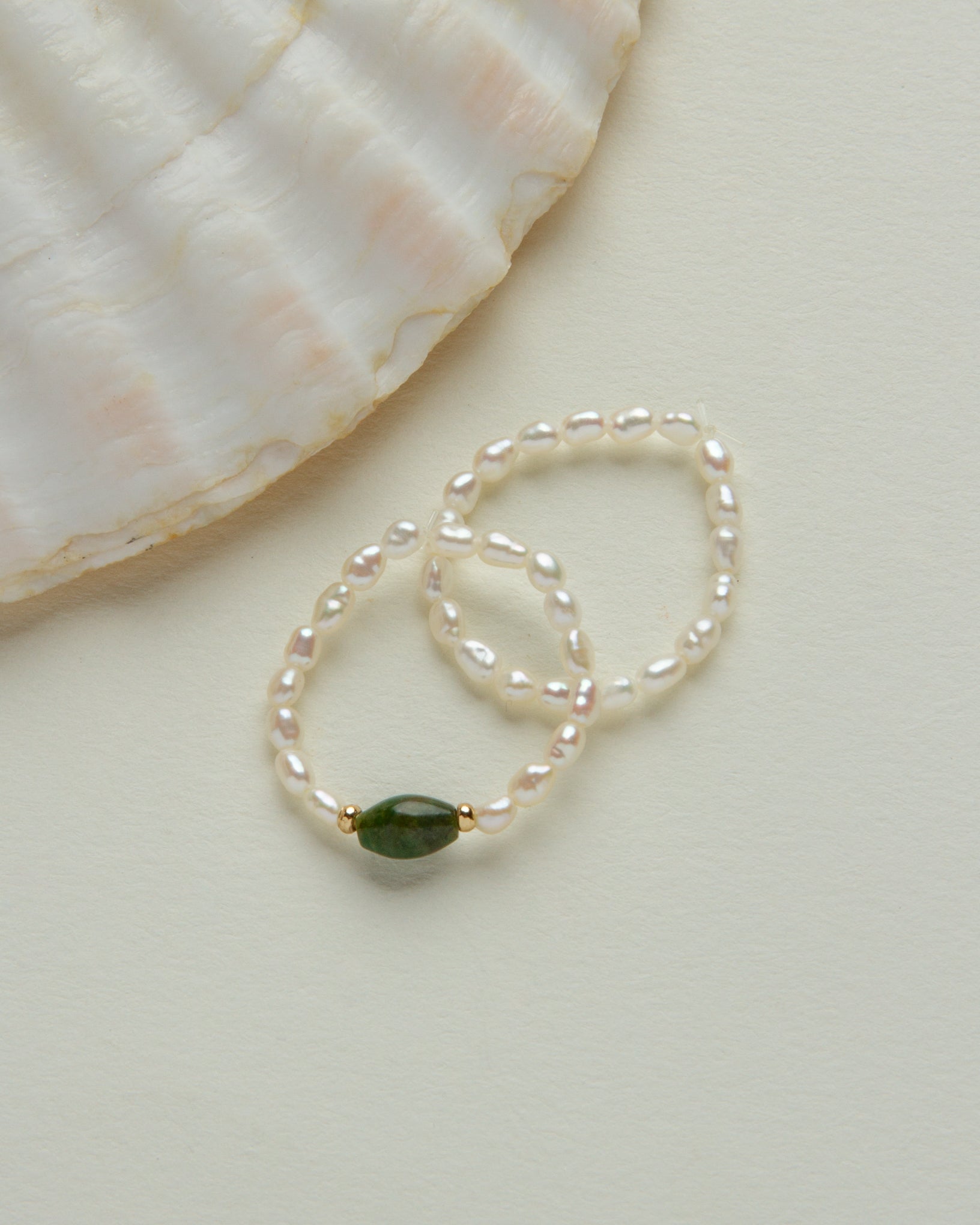Coastal Stretch Ring Set, featuring Freshwater Pearl and a green gemstone, beside a shell.