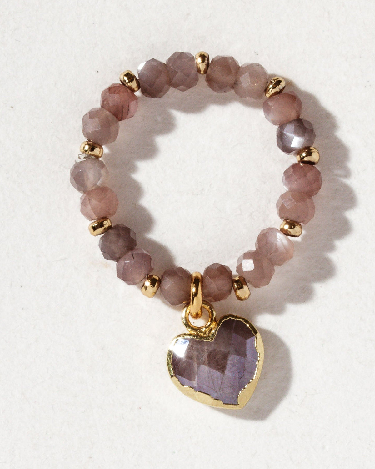 A stretch ring with a coffee moonstone dangling heart charm centerpiece and gold beads