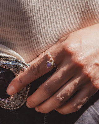 The model is wearing a gold ring on their index finger with a coffee moonstone heart-shaped stone.
