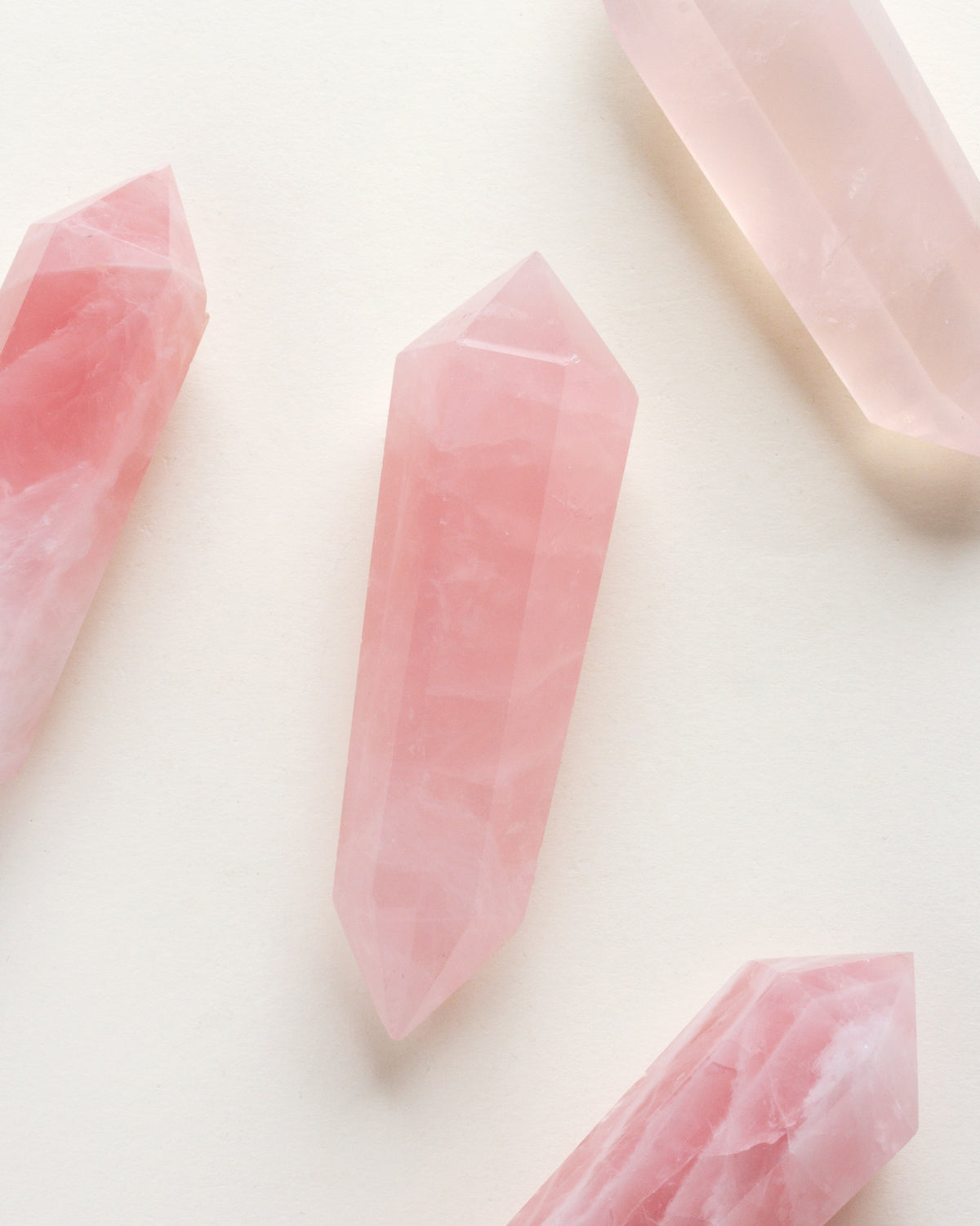 Rose Quartz double point crystals are arranged on a cream colored surface.