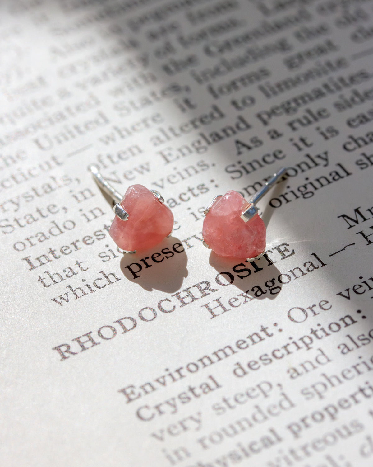 Pink Rhodochrosite post earrings on a book page with text.