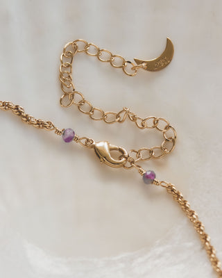 Gold chain necklace with a crescent moon charm and amethyst beads on a light background