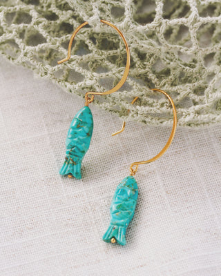 Turquoise fish-shaped earrings on a textured surface