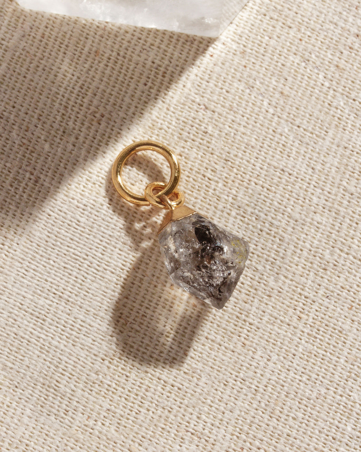 Single herkimer quartz gold hoop earring on a textured white surface.